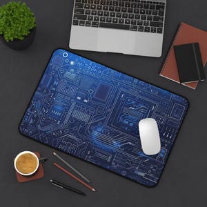 Puede incluir: Una alfombrilla de ratón de diseño de circuito azul y blanco con un ratón de ordenador blanco encima. La alfombrilla de ratón está sobre una superficie gris oscuro con un portátil, una taza de café y lápices.