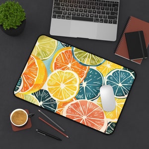 May include: A colorful mousepad with a pattern of overlapping citrus fruits in shades of yellow, orange, green, and blue. The mousepad is on a black surface with a laptop, a cup of coffee, and a notebook.