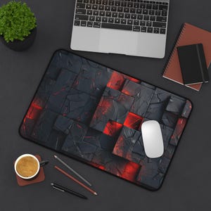 May include: A black and red gaming mouse pad with a textured, cracked stone design. The mouse pad is on a black surface with a laptop, a cup of coffee, and pencils.