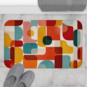 Può includere: Un tappetino da bagno rettangolare con un design geometrico retrò. Il tappetino presenta un motivo di quadrati e rettangoli arrotondati nei toni del rosso, arancione, giallo, verde acqua e rosa, su uno sfondo bianco sporco. Pantofole grigie in basso.