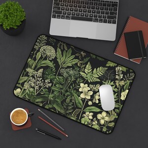 Può includere: Un tappetino per mouse nero con un motivo floreale verde e bianco. Il tappetino per mouse è su una superficie nera con un laptop, una tazza di caffè e matite.