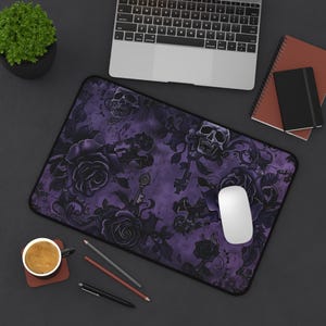 May include: Purple and black mouse mat with a skull and rose design. The mouse mat is on a black surface with a laptop, a cup of coffee, and pencils.