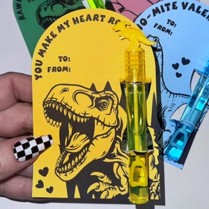 May include: A yellow dinosaur-shaped bubble wand with a yellow and green bubble solution bottle. The card reads "You make my heart roar" with a black and yellow dinosaur illustration. The card has a space to write "To:" and "From:".