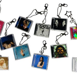 May include: A collection of ten miniature square keychains, each featuring a clear plastic case resembling a CD jewel box. The inserts display various album cover art, including images of musicians and text like My Chemical Romance and Sidequest.