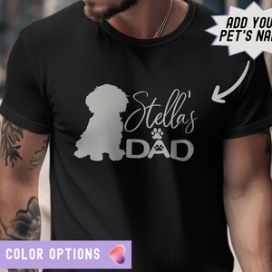 May include: Black t-shirt with a white silhouette of a dog and the text "Stella's Dad" in white. The text "Add Your Pet's Name" is in a speech bubble.