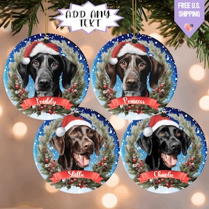 May include: Four round Christmas ornaments featuring dog portraits wearing Santa hats. Each ornament has a different dog breed, name, and a festive wreath design. The ornaments are hanging from a Christmas tree branch.