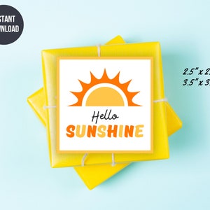 Puede incluir: Una pegatina cuadrada blanca con un sol amarillo y naranja y las palabras "Hello SUNSHINE" se coloca encima de dos regalos envueltos en amarillo. La pegatina está disponible en tamaños de 6,35 cm x 6,35 cm y 8,89 cm x 8,89 cm. Las palabras "INSTANT DOWNLOAD" están en un círculo negro.