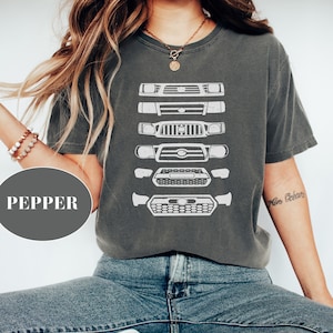 May include: A charcoal grey t-shirt with a graphic of a series of Toyota Tacoma front grilles printed in white. The shirt has a crew neck and short sleeves.