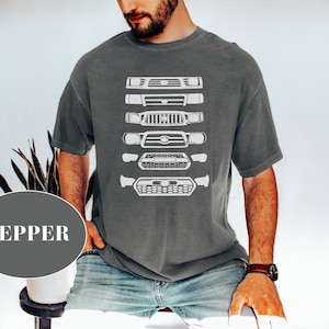 May include: A dark grey t-shirt with a white graphic of a series of Toyota Tacoma front ends. The graphic shows the evolution of the Tacoma front end from older models to newer models.