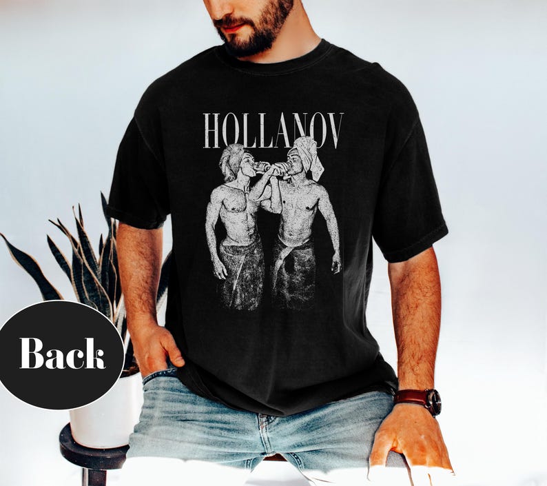 May include: Black t-shirt with the word "HOLLANOV" in white, above a black and white illustration of two figures. The figures are depicted in a vintage style, with one figure appearing to pour liquid into the other's mouth.