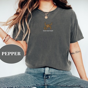 May include: A dark gray t-shirt with a small graphic of a stylized figure and the text "AMAZE AMAZE AMAZE" in brown. The shirt is paired with blue jeans. The word "PEPPER" is in a gray circle in the image.
