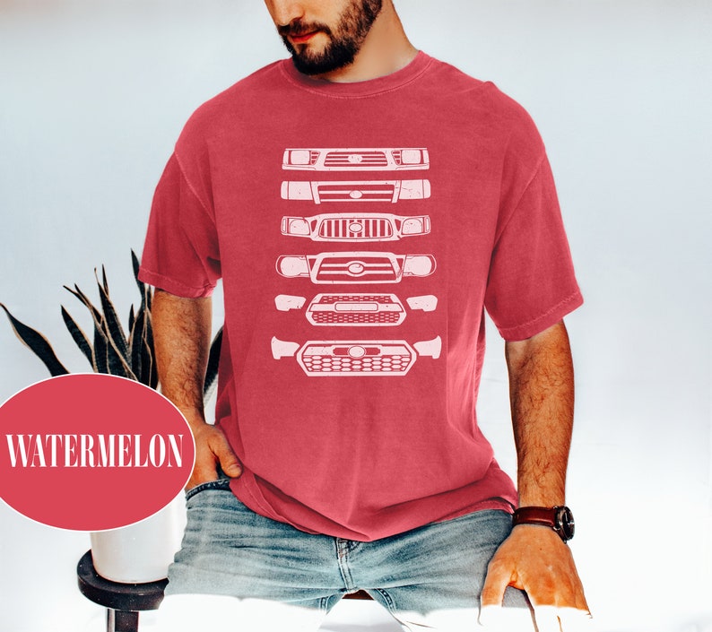 May include: A red t-shirt with a white graphic of a lineup of different Toyota Tacoma front grilles.