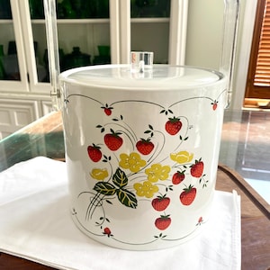 May include: White ice bucket with a clear plastic handle and a strawberry and flower design. The bucket has a white lid with a clear plastic knob.