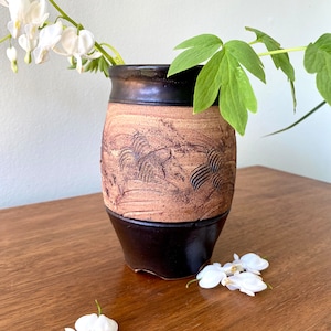 Peut inclure: Un vase en céramique brun et noir avec un motif texturé. Le vase est rempli de fleurs blanches et de feuilles vertes.