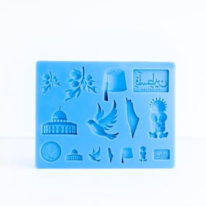 Puede incluir: Un molde de silicona azul claro con varias formas en relieve, incluyendo ramas de olivo, un fez, una estructura de cúpula, una paloma en vuelo, el contorno de un mapa, una figura estilizada y una placa con texto árabe y PALESTINE.
