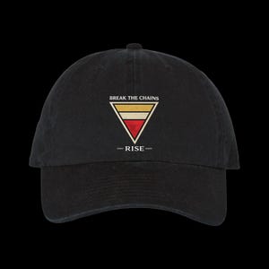 Puede incluir: Gorra de béisbol negra con un diseño triangular. El texto "BREAK THE CHAINS" está arriba y "-RISE-" abajo del triángulo. El triángulo tiene colores oro, rojo y blanco. La gorra está hecha de una tela suave y texturizada.