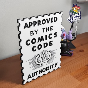 Puede incluir: Un letrero blanco con texto negro que dice "APPROVED BY THE COMICS CODE AUTHORITY". El letrero tiene un borde negro con un borde festoneado. Una figura con temática de cómic es visible en el fondo.
