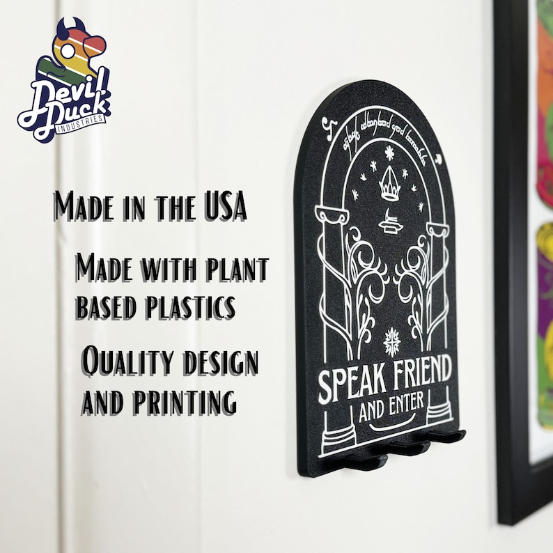 May include: Black key holder shaped like a door with the words "Speak Friend and Enter" and a design of a tree with a crown above it. The key holder is made in the USA with plant-based plastics.