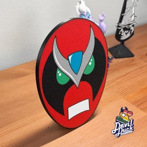 Könnte beinhalten: Runde, rot-schwarze Grafik mit einem stilisierten Eulen-Gesicht. Die Augen der Eule sind grün, der Schnabel weiß. Die Grafik hat einen schwarzen Rand und befindet sich auf einer Holzoberfläche. Das Logo von Devil Duck Industries befindet sich unten rechts.