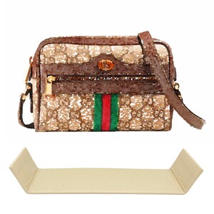 Peut inclure: Un sac à bandoulière marron et beige à motif avec une bandoulière en cuir marron et un détail de bande verte et rouge. Le sac a une fermeture éclair dorée et une boucle dorée.