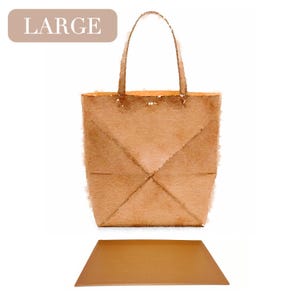 Puede incluir: Un bolso tote grande de color marrón con una base de cuero marrón. El bolso tiene un diseño sencillo con un solo asa.
