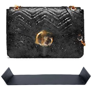 Peut inclure: Un sac à main noir matelassé avec un accent circulaire doré. Le sac a une bandoulière noire.