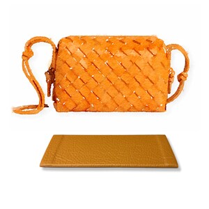 Könnte beinhalten: Eine geflochtene orangefarbene Ledertasche mit einem langen Riemen. Die Tasche liegt auf einer passenden orangefarbenen Lederoberfläche.