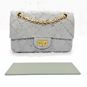 May include: A gray quilted handbag with a gold chain strap and a gold clasp. The bag is sitting on a light gray surface.