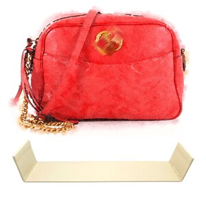 Peut inclure: Un sac à bandoulière en cuir rouge avec une bandoulière en chaîne dorée et un logo circulaire doré sur le devant.