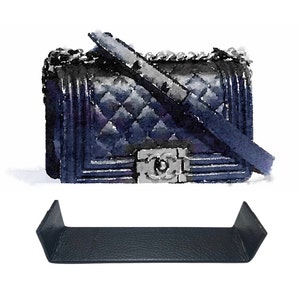 May include: A black quilted leather handbag with a silver chain strap and a silver clasp. The bag is sitting on a black leather shelf.