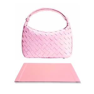 May include: A pink woven leather handbag with a single strap. The handbag is sitting on a pink leather mat.