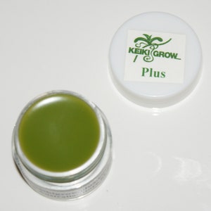 May include: A small, clear jar containing a green, thick, balm-like substance. The jar has a white lid with a green logo that says "KEIKI GROW Plus".