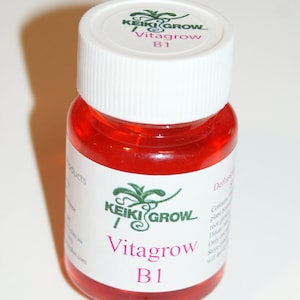 May include: A small, clear bottle containing a bright red liquid. The white label displays "KEIKI GROW Vitagrow B1" in green and pink. The bottle has a white cap with the same logo and text.