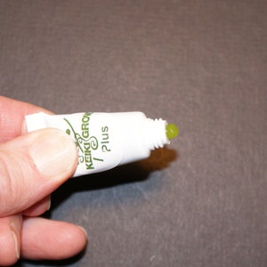 Puede incluir: Un tubo blanco con una etiqueta verde que dice "Keiki Grow Plus" y una sustancia gelatinosa verde que sale de la punta.