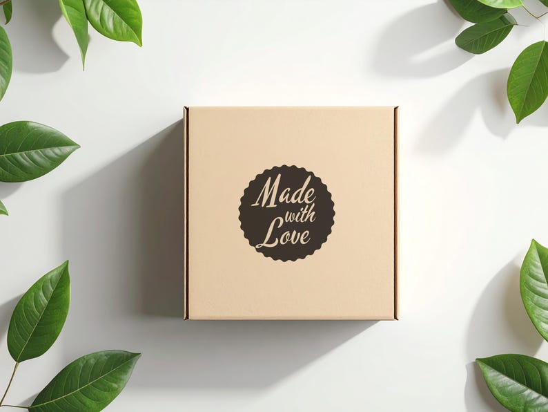 Peut inclure: Une bo&icirc;te carr&eacute;e en carton brun clair avec l'inscription "Made with Love" dans un motif circulaire marron fonc&eacute;. La bo&icirc;te est entour&eacute;e de feuilles vertes sur fond blanc.