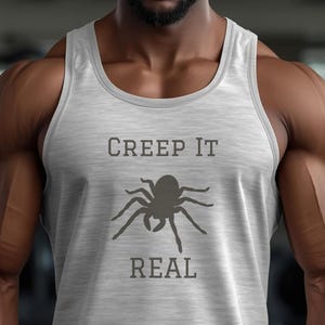 Peut inclure: D&eacute;bardeur gris clair avec l'inscription "CREEP IT REAL" en gris fonc&eacute; au-dessus et en dessous d'un dessin d'araign&eacute;e. Le d&eacute;bardeur est sans manches et en mati&egrave;re souple.