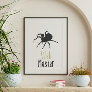 Peut inclure: Impression encadr&eacute;e avec une silhouette d'araign&eacute;e noire et les mots "Web Master". L'impression est dans un cadre noir, pos&eacute;e sur une &eacute;tag&egrave;re en bois avec des livres et une plante en pot. Le fond est de couleur neutre. Th&egrave;me d'Halloween.