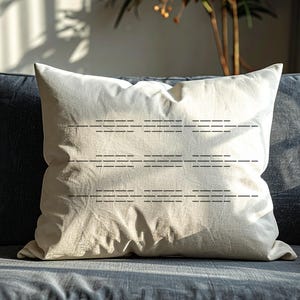 Puede incluir: Un coj&iacute;n decorativo cuadrado de color blanquecino con un dise&ntilde;o de l&iacute;neas horizontales cosidas. El coj&iacute;n est&aacute; colocado sobre un sof&aacute; gris oscuro. La tela del coj&iacute;n parece ser lino o un material similar.