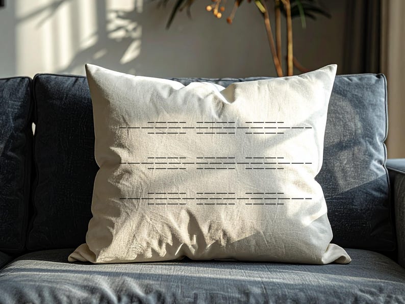 Puede incluir: Un coj&iacute;n decorativo cuadrado de color blanquecino con un dise&ntilde;o de l&iacute;neas horizontales cosidas. El coj&iacute;n est&aacute; colocado sobre un sof&aacute; gris oscuro. La tela del coj&iacute;n parece ser lino o un material similar.