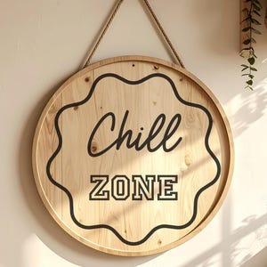 Peut inclure: Panneau rond en bois avec l'inscription "Chill ZONE" en noir. Le panneau est bord&eacute; d'un motif noir ondul&eacute; et est suspendu par une corde naturelle. Le bois a une finition claire et naturelle.
