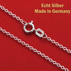 Könnte beinhalten: Eine Silberkette mit einem runden Federringverschluss und einem kleinen rechteckigen Anhänger, der mit der Zahl 925 geprägt ist. Der Text Echt Silber Made in Germany ist in der oberen rechten Ecke des Bildes zu sehen.