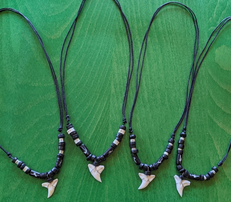 May include: Three black cord necklaces with white beads and a white shark tooth pendant.