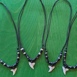 May include: Three black cord necklaces with white and black bead accents and a white shark tooth pendant.