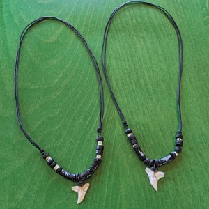 May include: Two black cord necklaces with black and silver beads and a white shark tooth pendant.