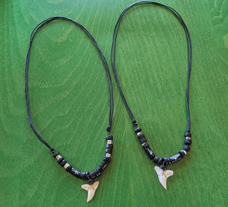 May include: Two black cord necklaces with black and silver beads and a white shark tooth pendant.