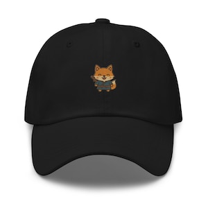 May include: Black baseball cap featuring an embroidered cartoon fox wearing a blue and orange outfit. The fox is holding a small object. The cap has a curved brim and a button on top.