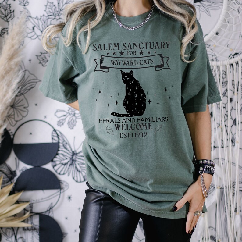 Może przedstawiać: Zielona koszulka z czarnym kotem i tekstem "Salem Sanctuary for Wayward Cats. Ferals and Familiars Welcome. Est. 1692."