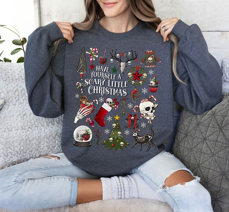 May include: A dark gray sweatshirt with a Christmas themed design. The design features a variety of festive elements including skulls, candy canes, Christmas trees, and a stocking. The text on the sweatshirt reads 'Have Yourself a Scary Little Christmas'.