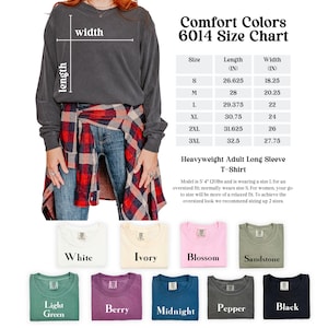 May include: A dark grey long-sleeved t-shirt with a size chart. The chart shows measurements in inches for sizes S to 3XL. Below are colour swatches in white, ivory, blossom, sandstone, light green, berry, midnight, pepper, and black.