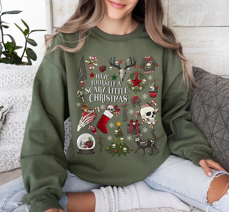 May include: Green sweatshirt with a festive, spooky Christmas design. It features skulls, candy canes, a Christmas tree, and the text "Have Yourself a Scary Little Christmas".